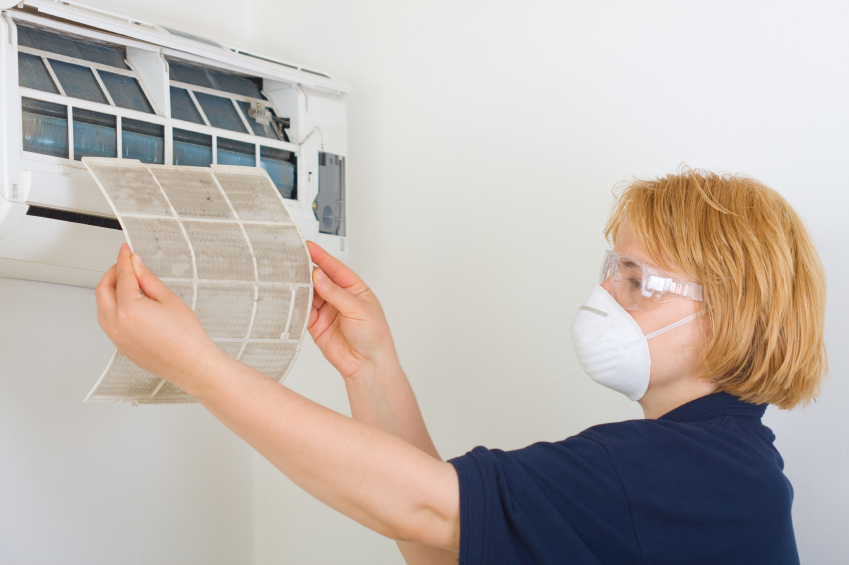 Person wearing safety goggles and a mask, cleaning a wall-mounted air conditioning unit.