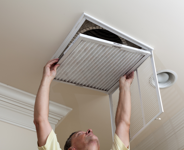 Person replacing an air filter in a ceiling vent.