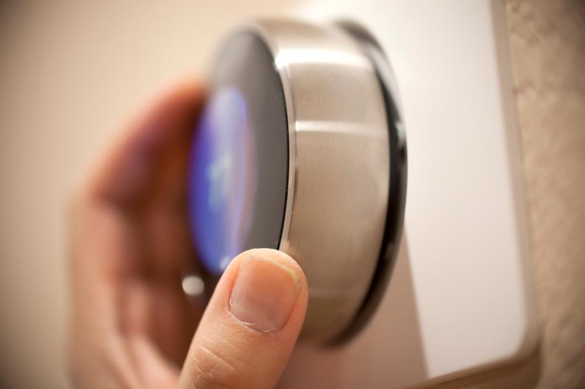 Close-up of a hand adjusting a metallic circular thermostat on a wall.