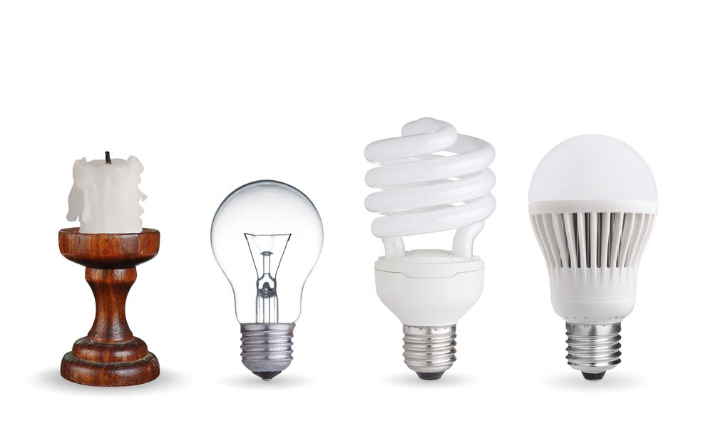 A candle, incandescent bulb, CFL bulb, and LED bulb displayed in a row.