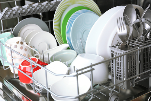 the interior of an open metallic dishwasher filled with clean dishes. The top rack is visible, exhibiting neatly arranged plates, bowls, cups, and cutlery. The plates vary in color, including white, green, blue, and patterned designs.