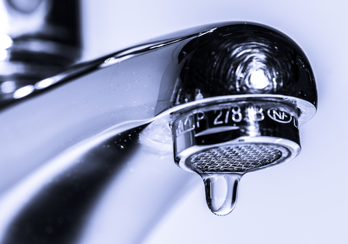 Close-up of a chrome faucet with a single water droplet hanging from the spout.