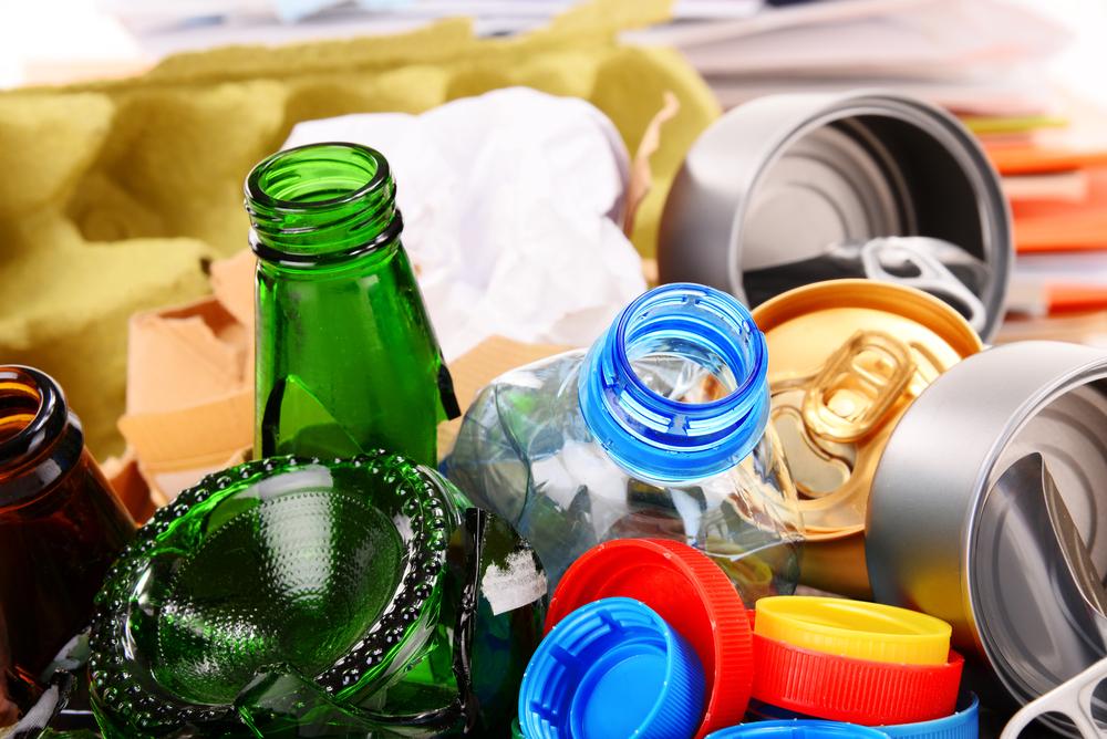 ixed recyclable materials including glass bottles, plastic bottles with colorful caps, and aluminum cans.