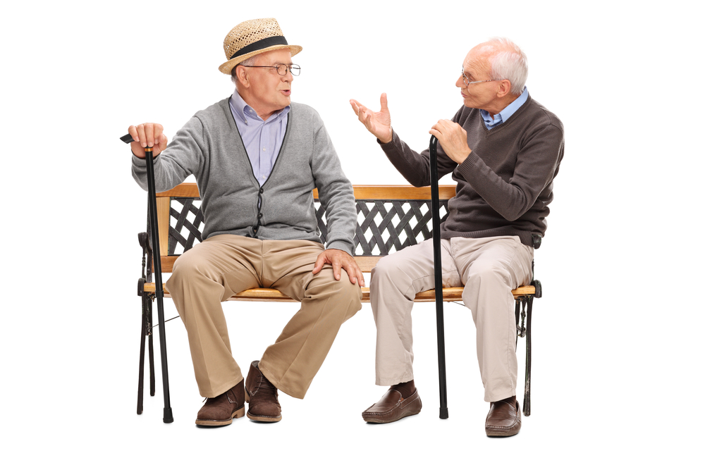 Two elderly men with canes seated on a bench, talking and gesturing.
