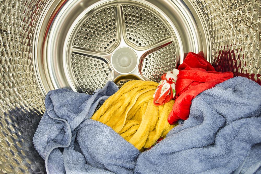 Washing machine drum with blue, yellow, and red towels inside.