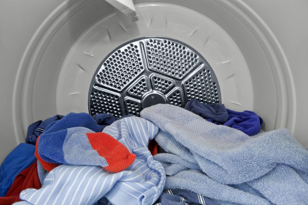 a close-up view of the interior of a tumble dryer, showing an assortment of laundry inside. The drum of the dryer is metallic and forms a semi-circular shape around the visible section. 